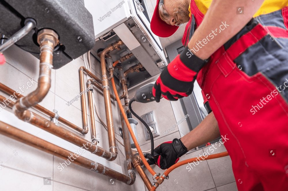 Plumber in work gloves connecting copper pipes to a water heater