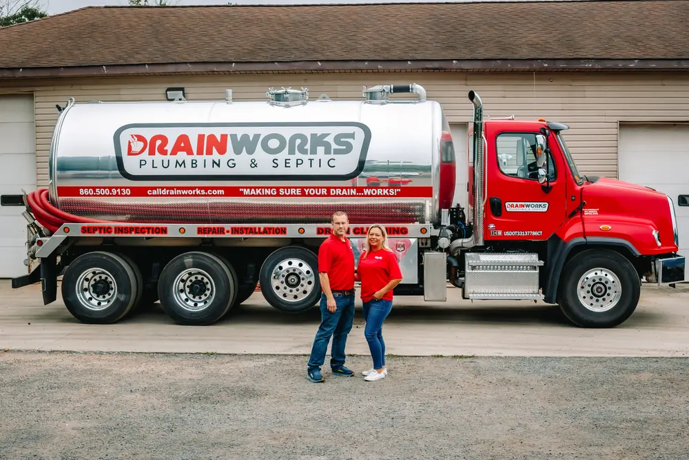 The Drainworks owners standing in front of their red septic pump truck